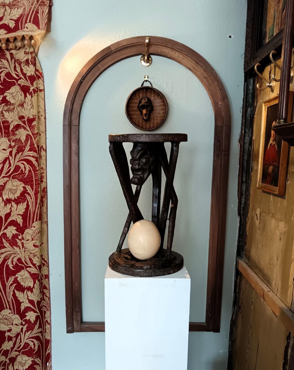 A dark carved timber side table featuring a circular top supported by a stylised crouching figure above a rounded base. View IX
