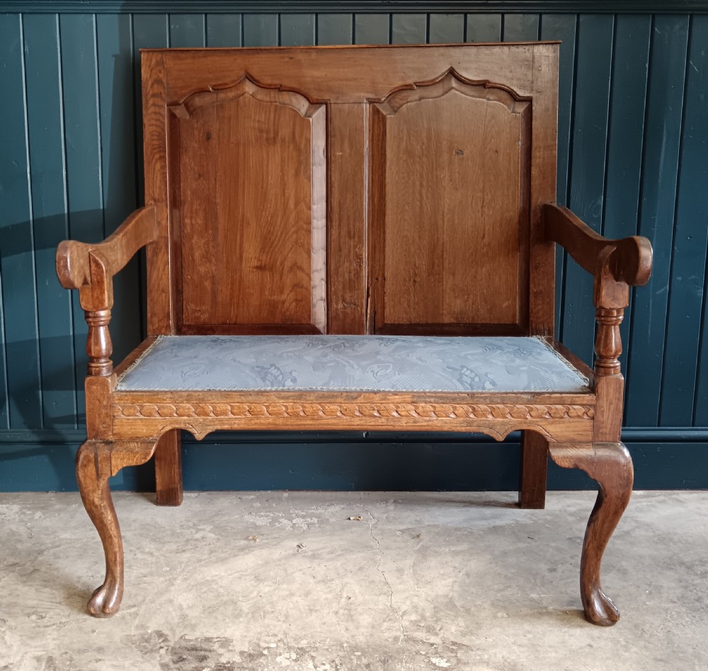 A Georgian oak two-seater settle bench with a twin-panelled back, cabriole front legs, and a blue patterned seat. View II