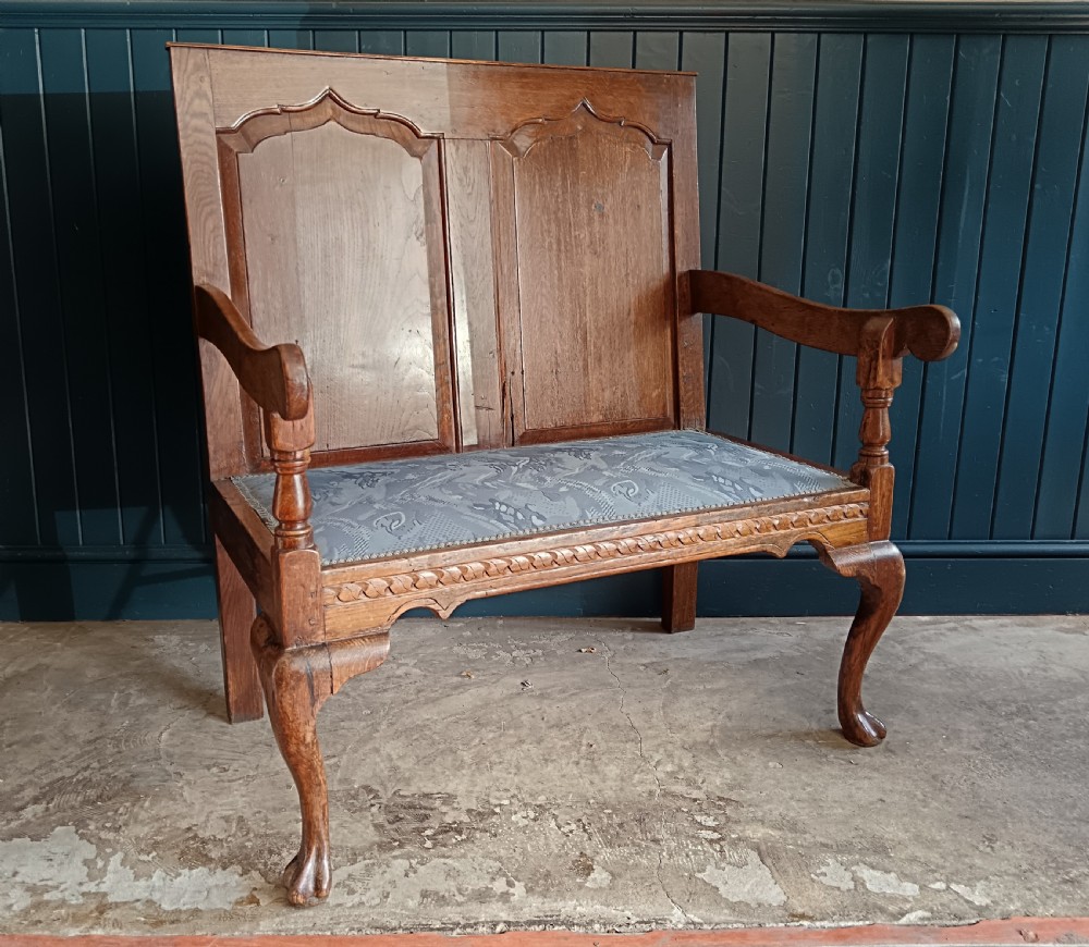 A Georgian oak two-seater settle bench with a twin-panelled back, cabriole front legs, and a blue patterned seat.