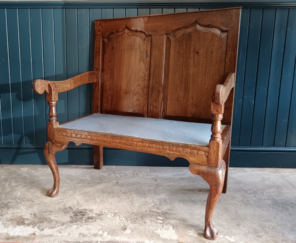 A Georgian oak two-seater settle bench with a twin-panelled back, cabriole front legs, and a blue patterned seat. View III