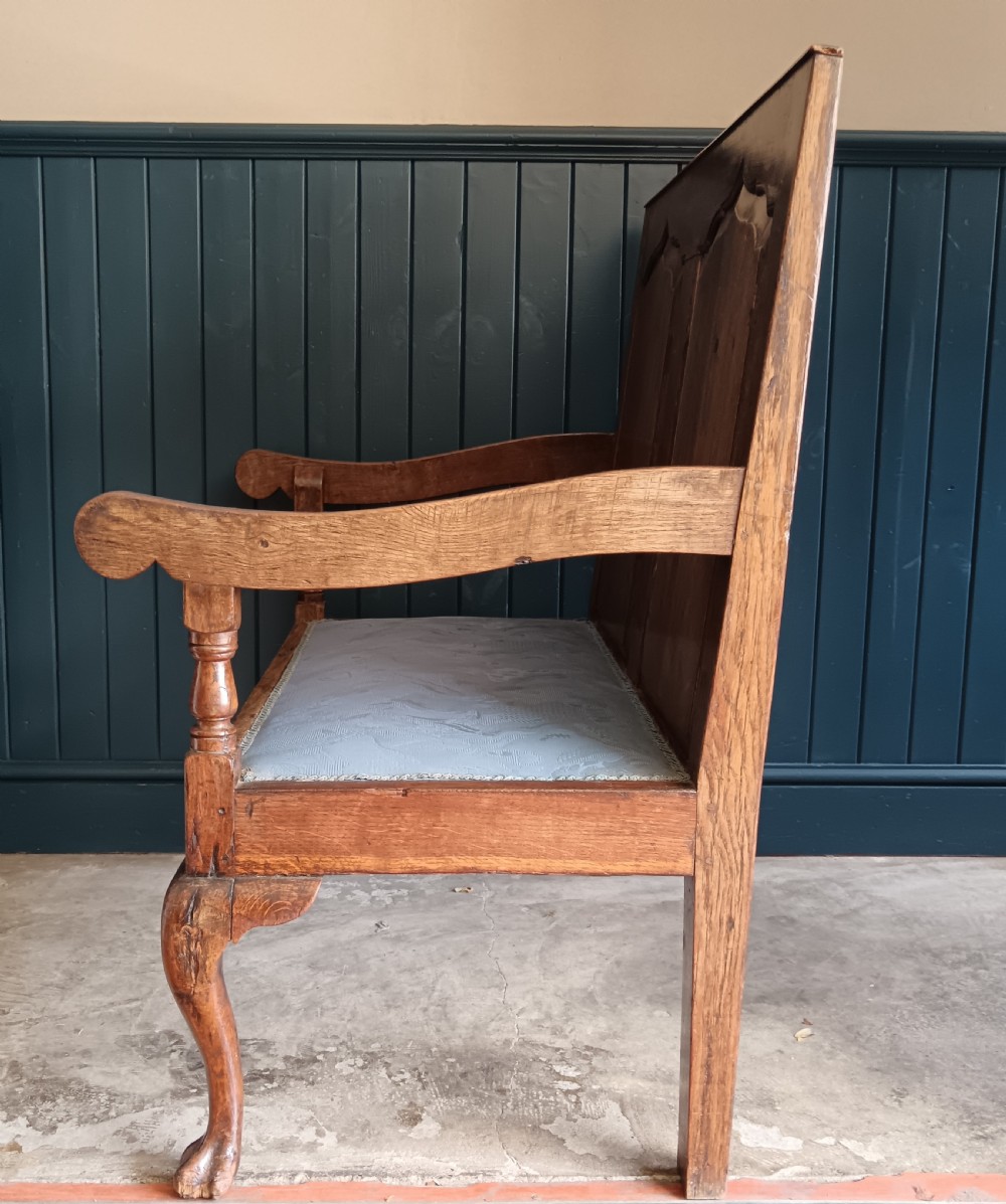 A Georgian oak two-seater settle bench with a twin-panelled back, cabriole front legs, and a blue patterned seat. View VIII