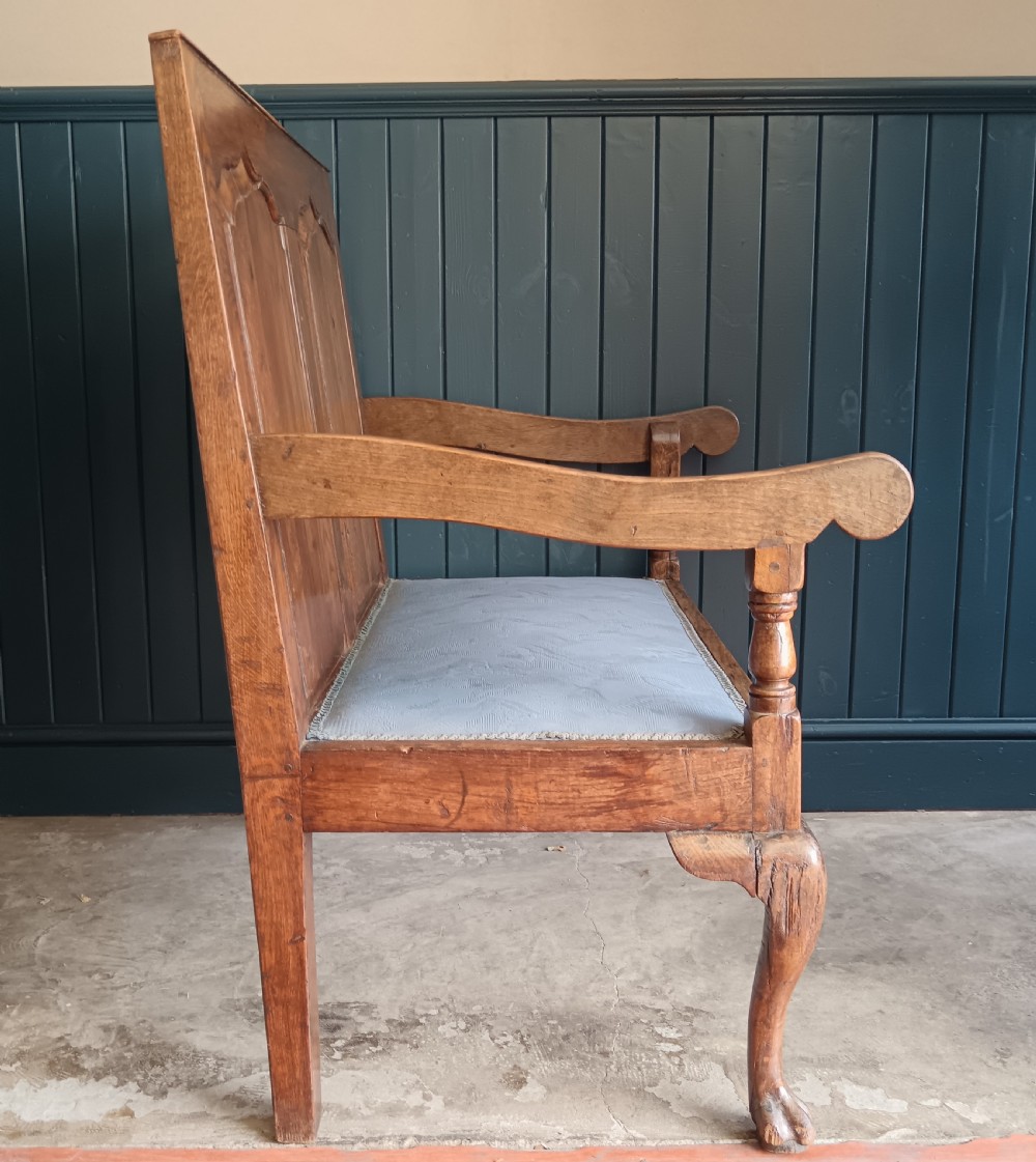 A Georgian oak two-seater settle bench with a twin-panelled back, cabriole front legs, and a blue patterned seat. View IX