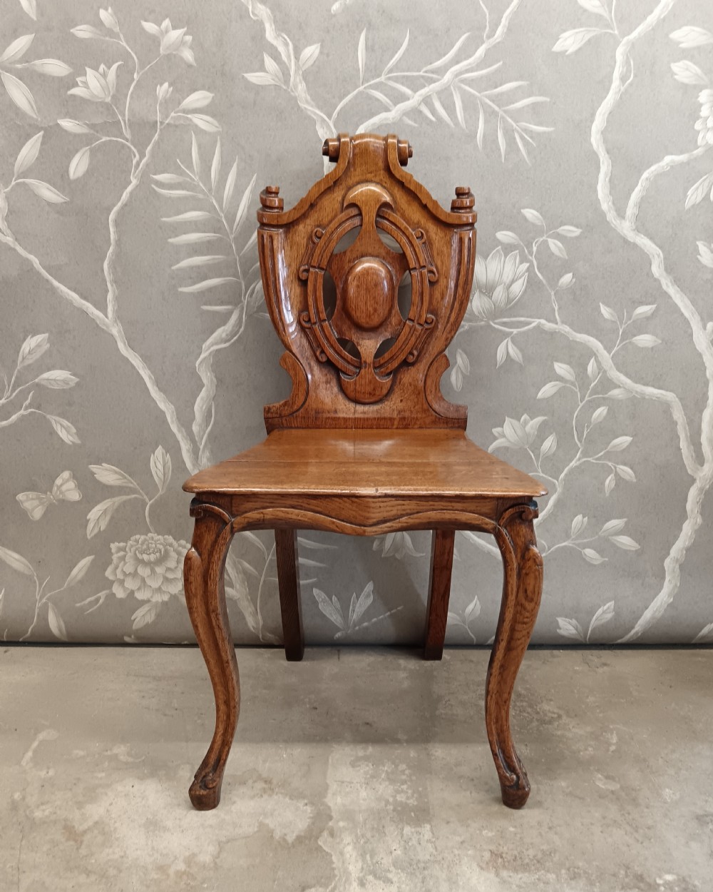 A Victorian carved oak hall chair featuring a relief cartouche backrest, solid wood seat, and cabriole front legs.