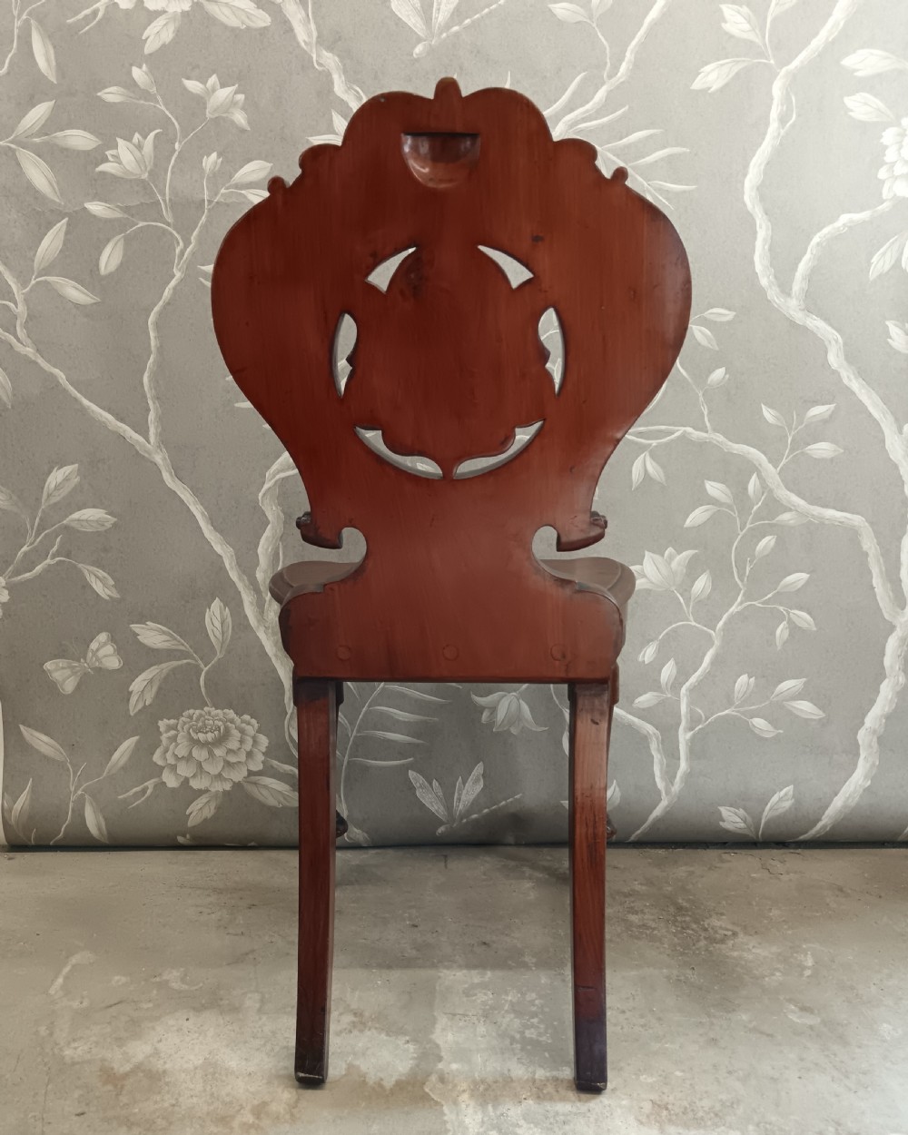 A Victorian mahogany hall chair featuring a carved scrollwork backrest with a central shield motif, a solid timber seat, and turned front legs. View VI