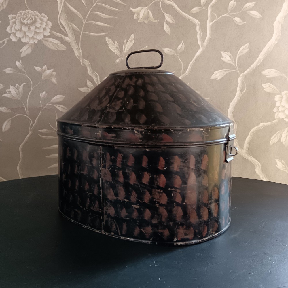 A dark painted antique tin hat box with a domed lid, top carrying handle, and hand-painted pattern. View VII