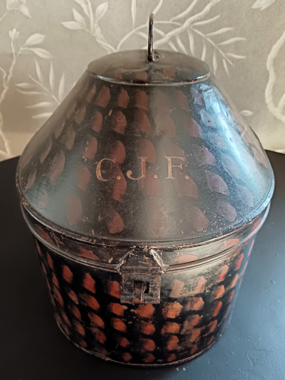 A dark painted antique tin hat box with a domed lid, top carrying handle, and hand-painted pattern. View II