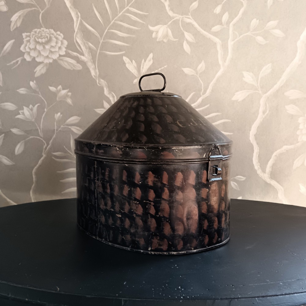 A dark painted antique tin hat box with a domed lid, top carrying handle, and hand-painted pattern. View VI