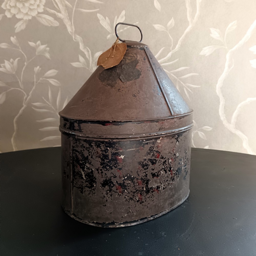An antique oval black toleware tin military hat box featuring a tall conical lid and a top loop handle.