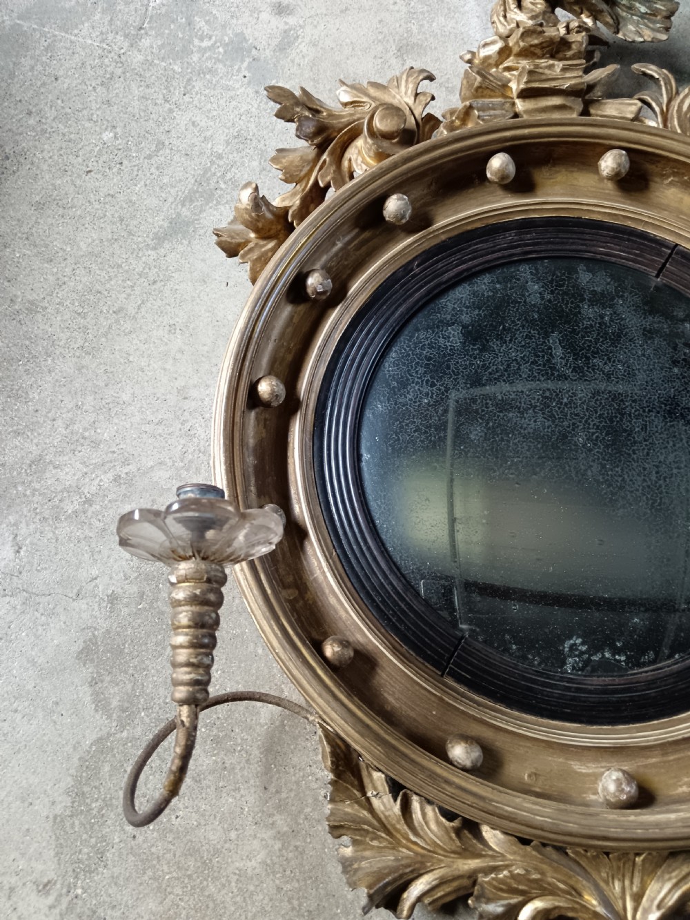 A circular Regency style giltwood convex wall mirror topped with a carved eagle cresting and featuring twin candle sconces. View III