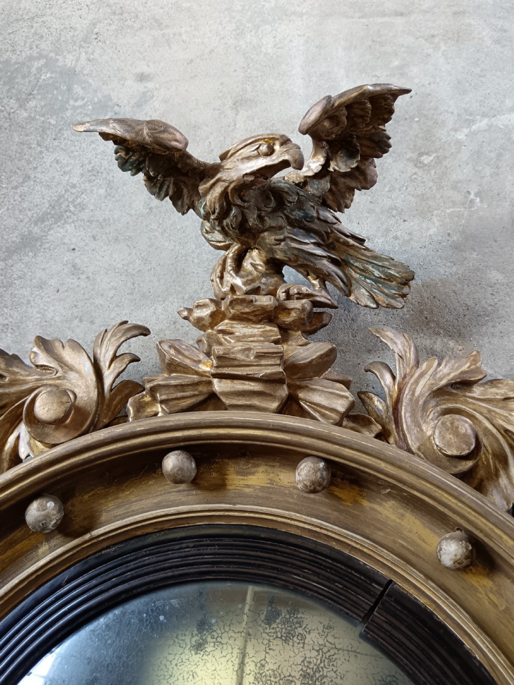 A circular Regency style giltwood convex wall mirror topped with a carved eagle cresting and featuring twin candle sconces. View X