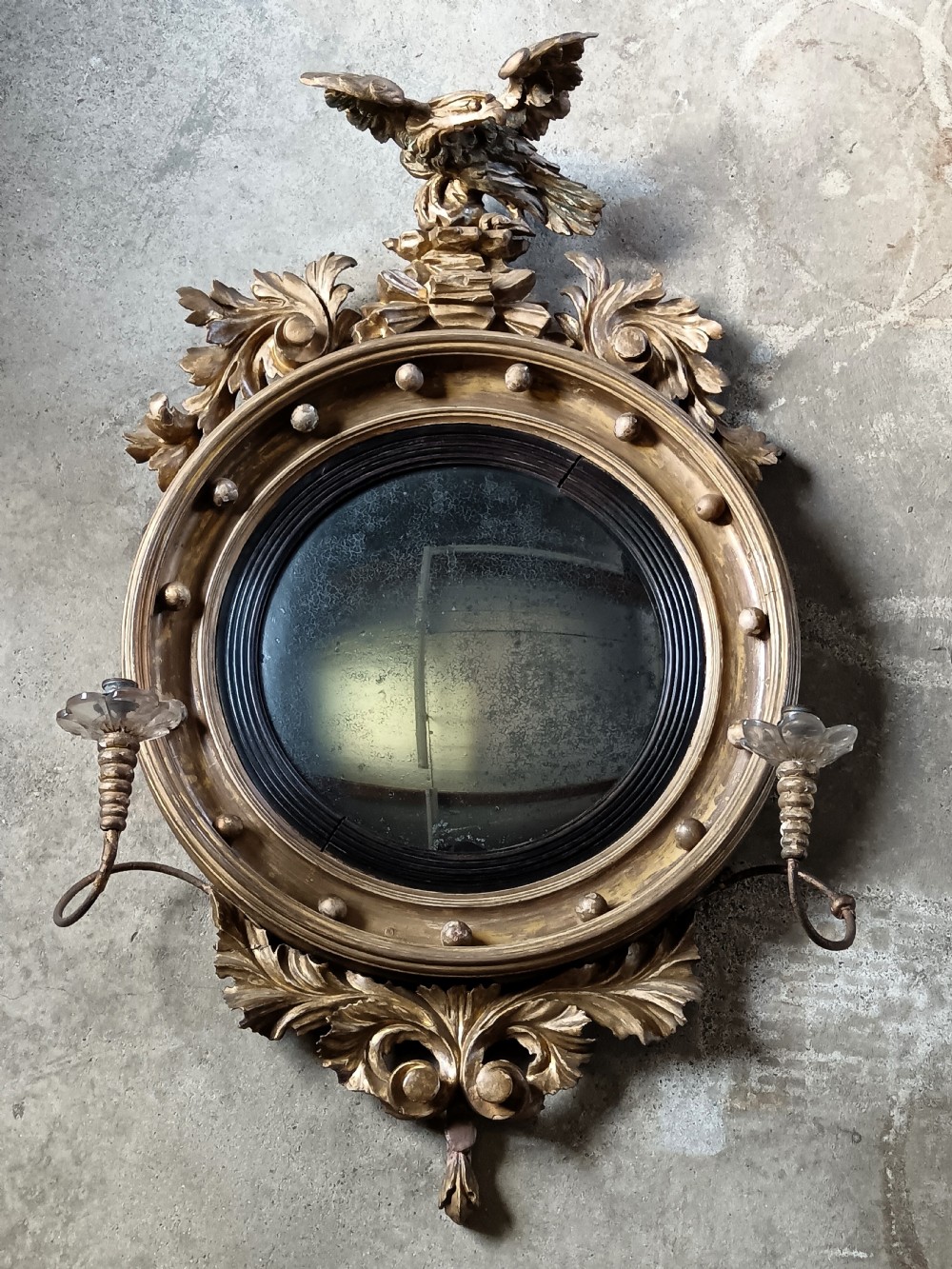 A circular Regency style giltwood convex wall mirror topped with a carved eagle cresting and featuring twin candle sconces. View VII