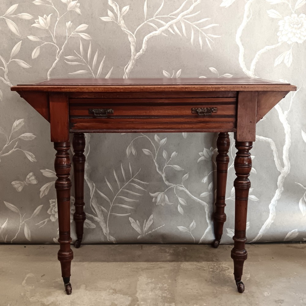 An Arts and Crafts mahogany writing desk featuring a brown leather inset top, a single wide drawer with metal handles, turned legs, and brass castors.