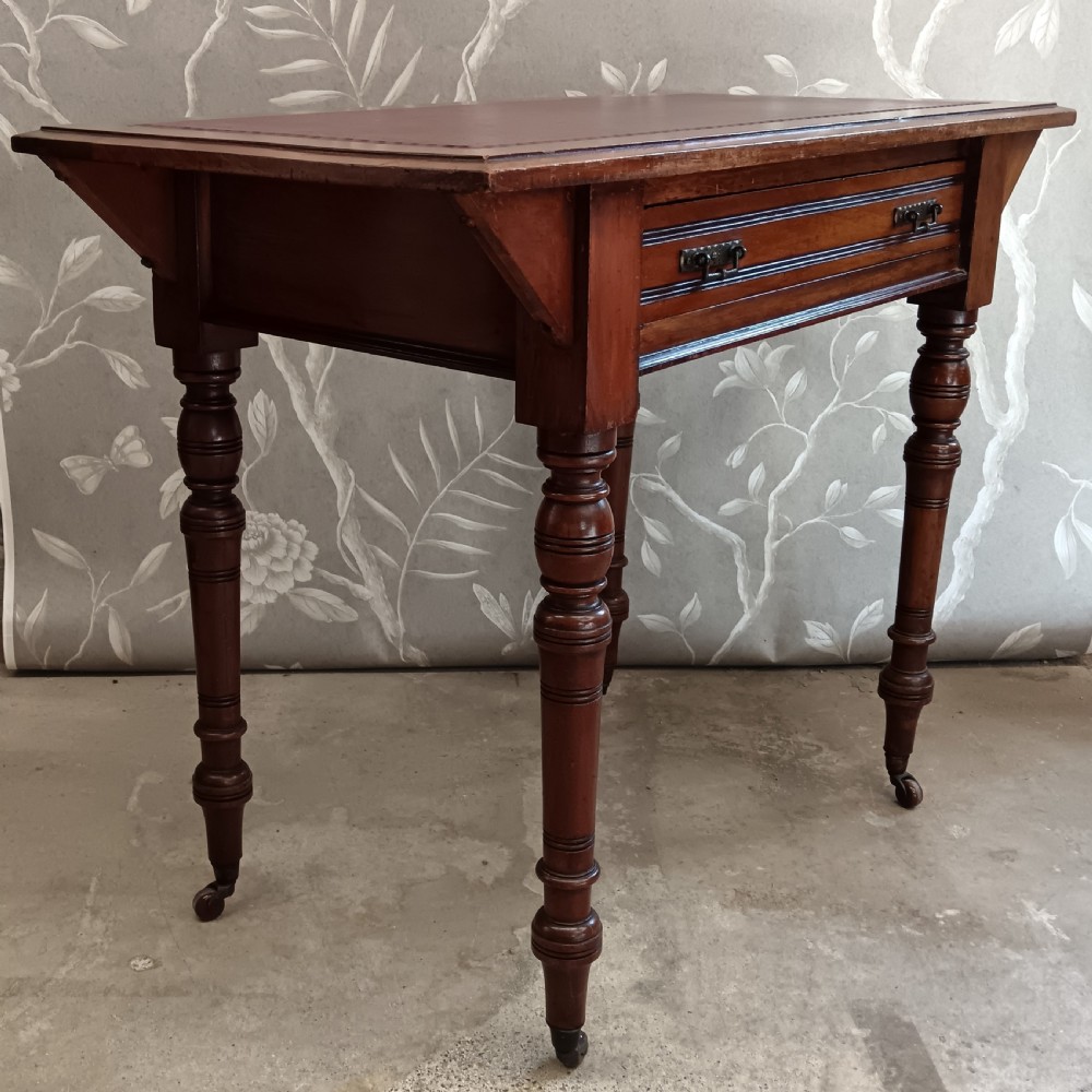 An Arts and Crafts mahogany writing desk featuring a brown leather inset top, a single wide drawer with metal handles, turned legs, and brass castors. View III