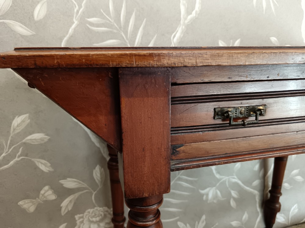 An Arts and Crafts mahogany writing desk featuring a brown leather inset top, a single wide drawer with metal handles, turned legs, and brass castors. View VII