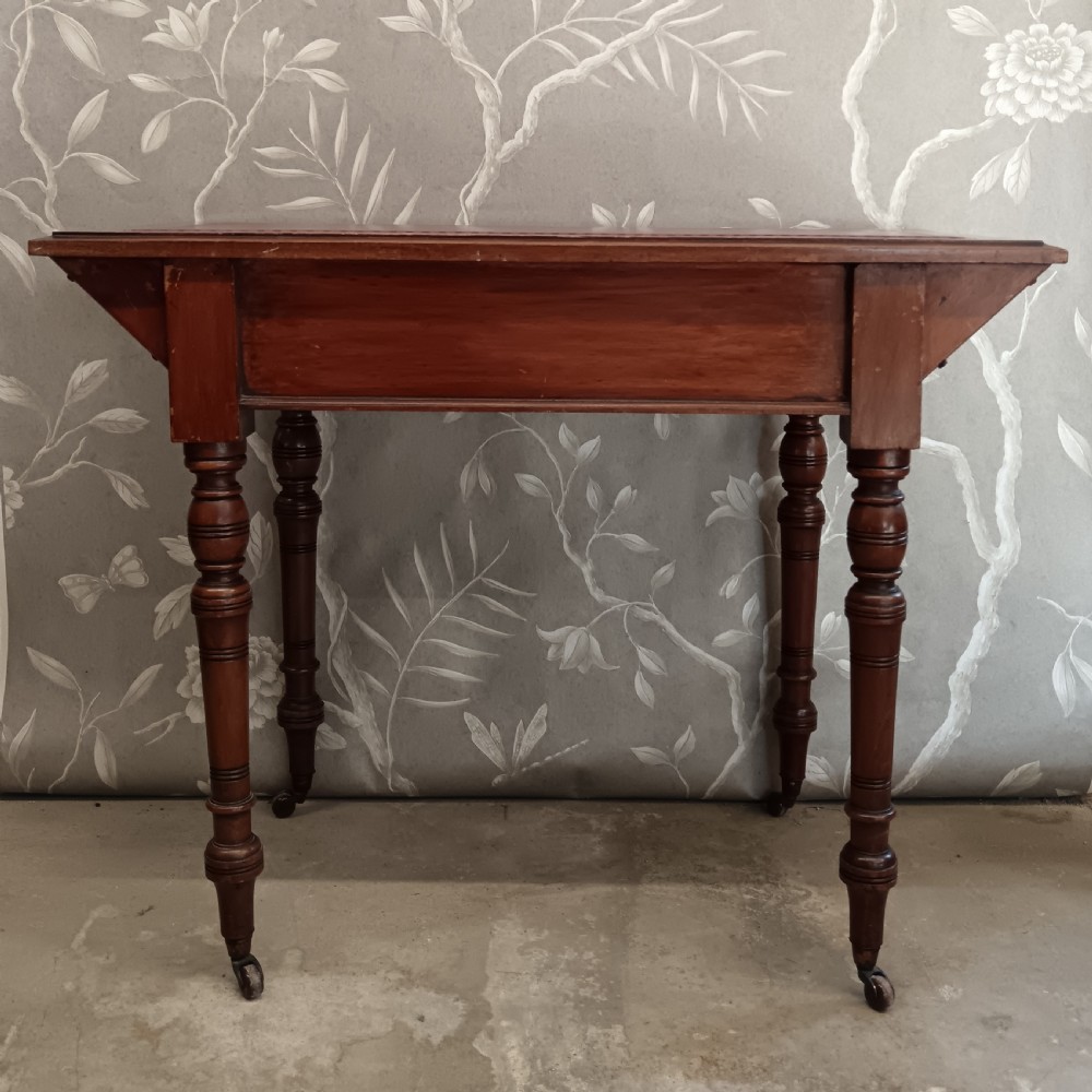 An Arts and Crafts mahogany writing desk featuring a brown leather inset top, a single wide drawer with metal handles, turned legs, and brass castors. View VIII