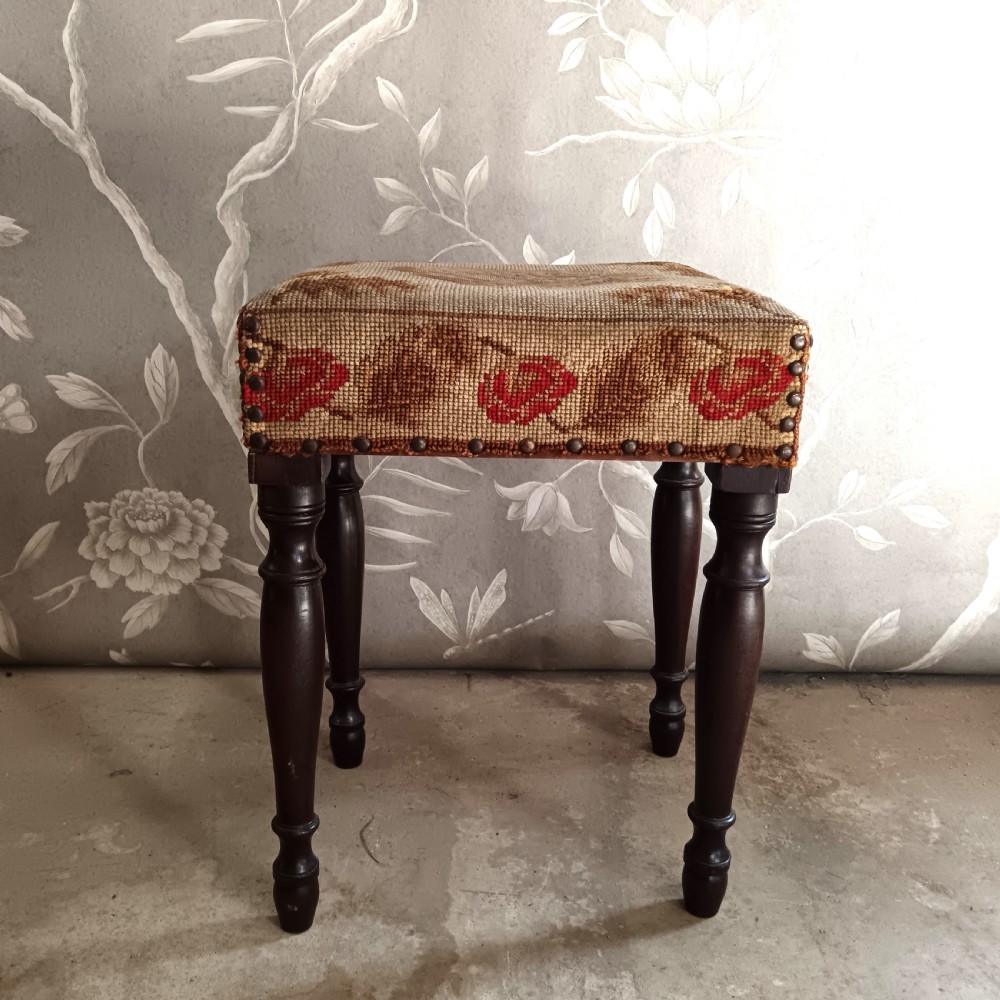 A rectangular Victorian mahogany stool featuring dark turned legs and a tapestry top with red floral rose motifs bordered by brass studs.