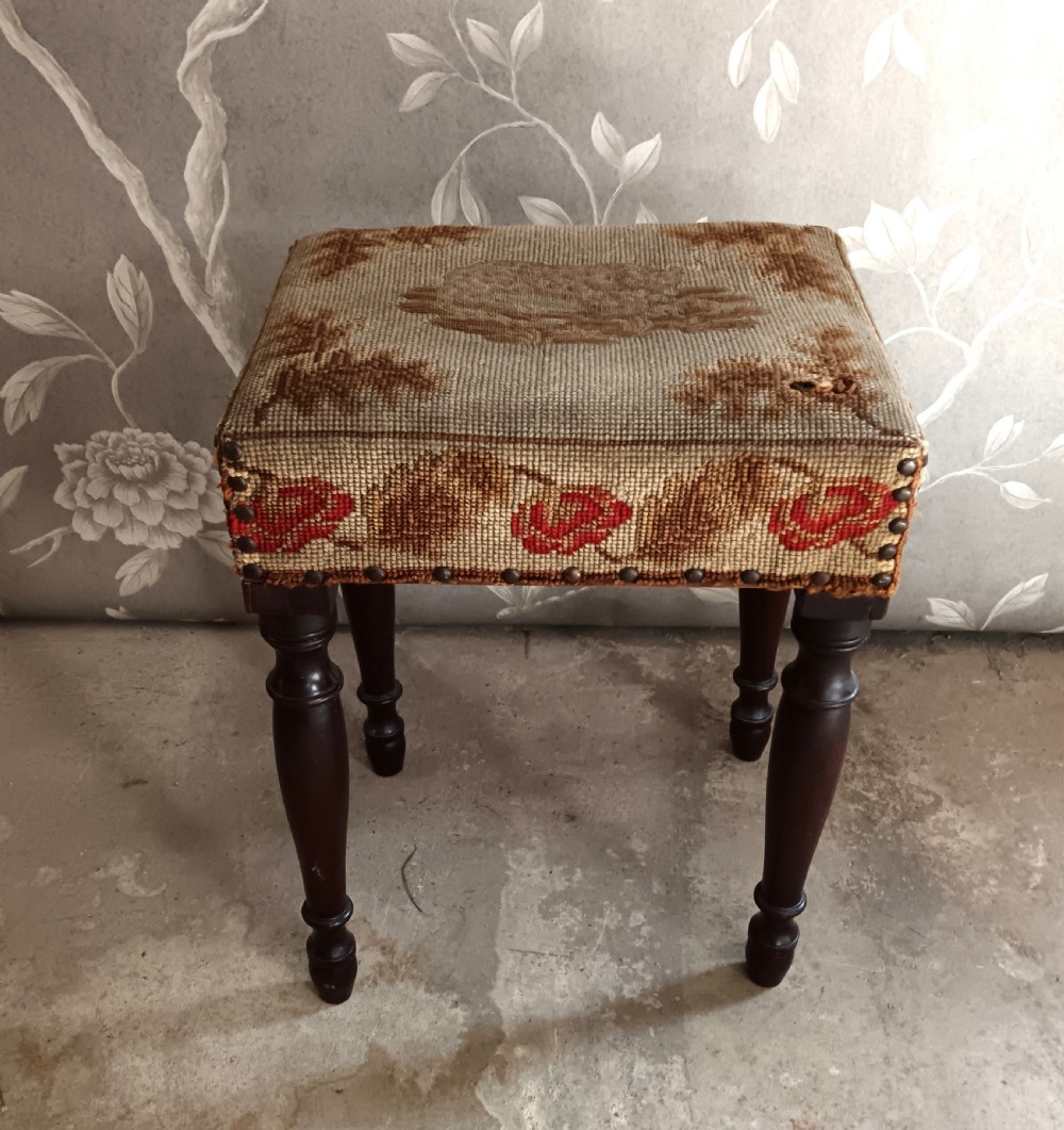 A rectangular Victorian mahogany stool featuring dark turned legs and a tapestry top with red floral rose motifs bordered by brass studs. View II