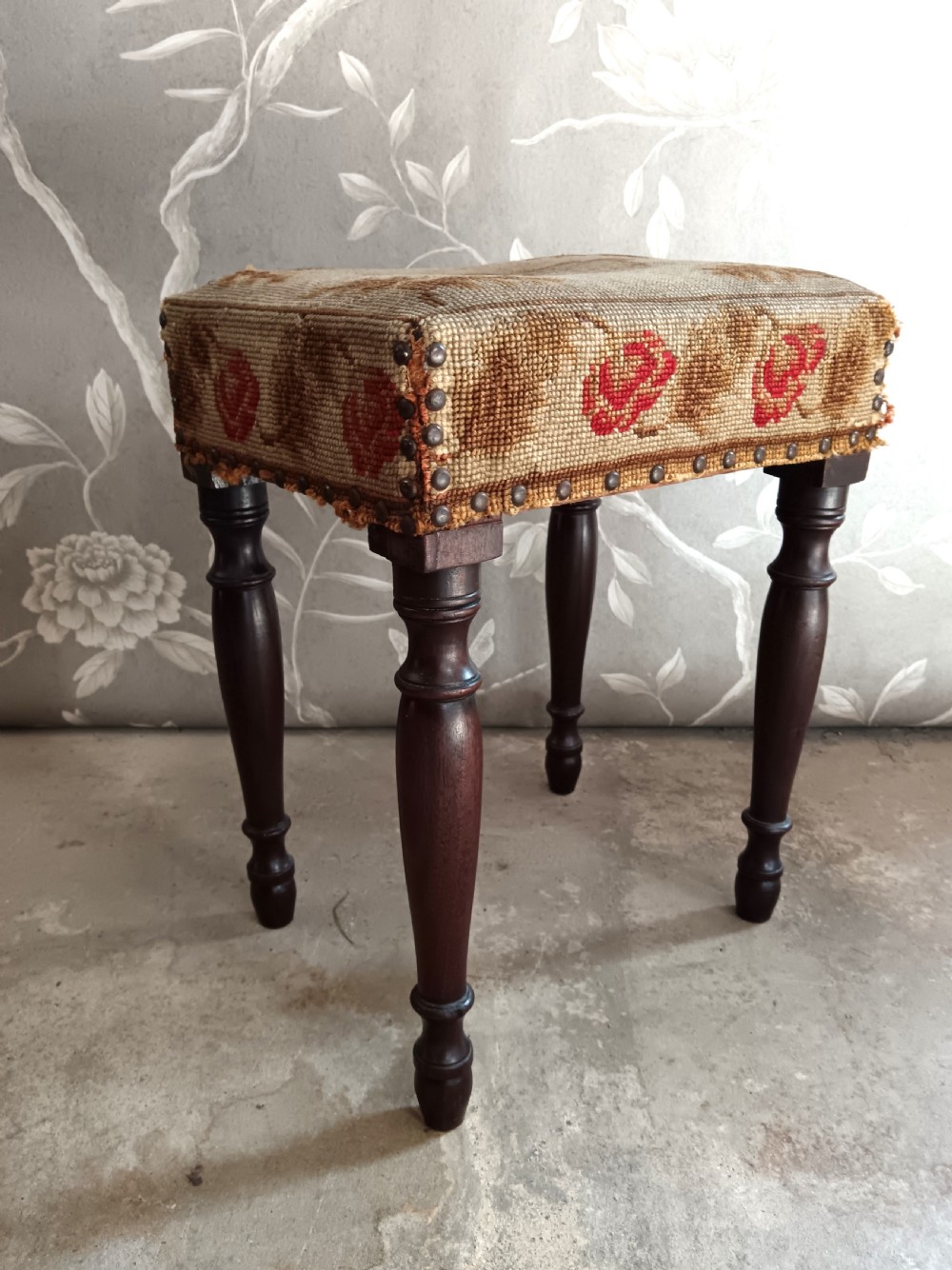 A rectangular Victorian mahogany stool featuring dark turned legs and a tapestry top with red floral rose motifs bordered by brass studs. View VI