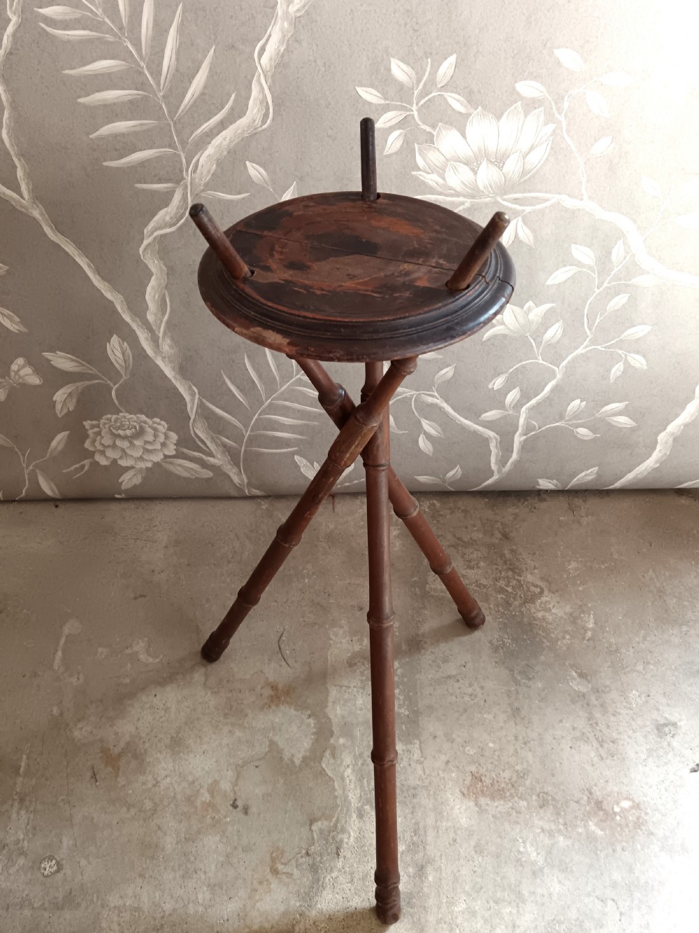 A dark brown wooden campaign washbowl stand featuring turned faux-bamboo tripod legs and vertical pegs around a circular top. View V