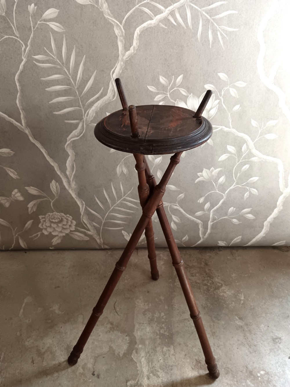 A dark brown wooden campaign washbowl stand featuring turned faux-bamboo tripod legs and vertical pegs around a circular top. View VI