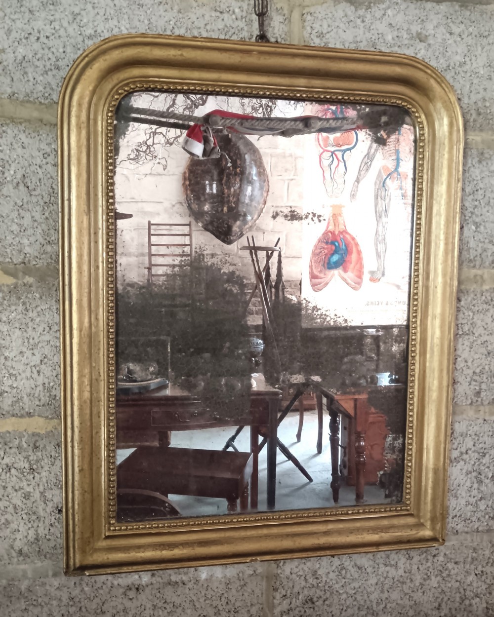 A 19th-century French wall mirror featuring a rectangular gilded frame with rounded upper corners, beaded interior moulding, and heavily foxed glass.