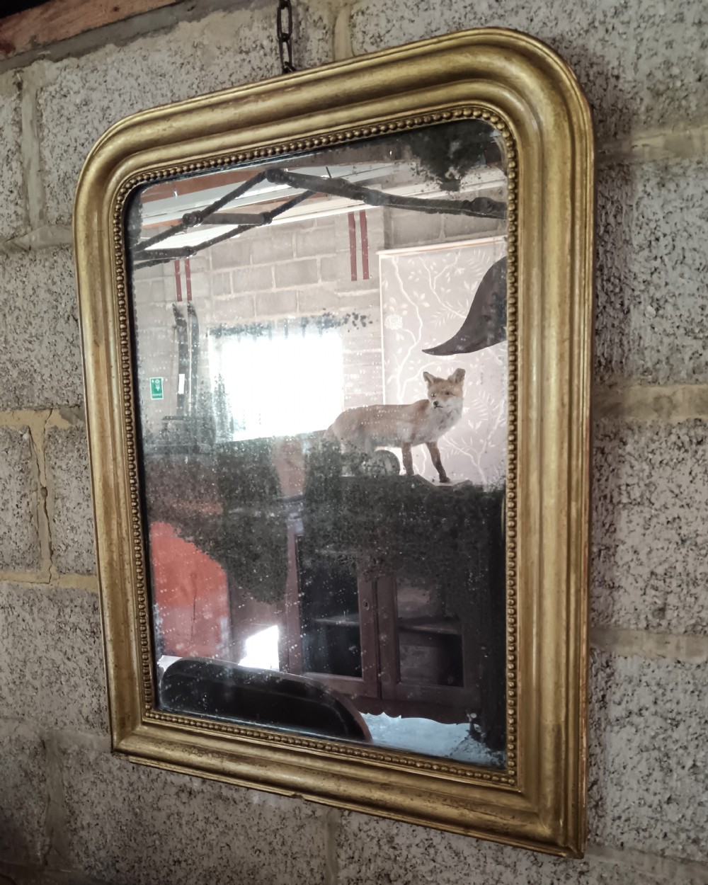 A 19th-century French wall mirror featuring a rectangular gilded frame with rounded upper corners, beaded interior moulding, and heavily foxed glass. View II