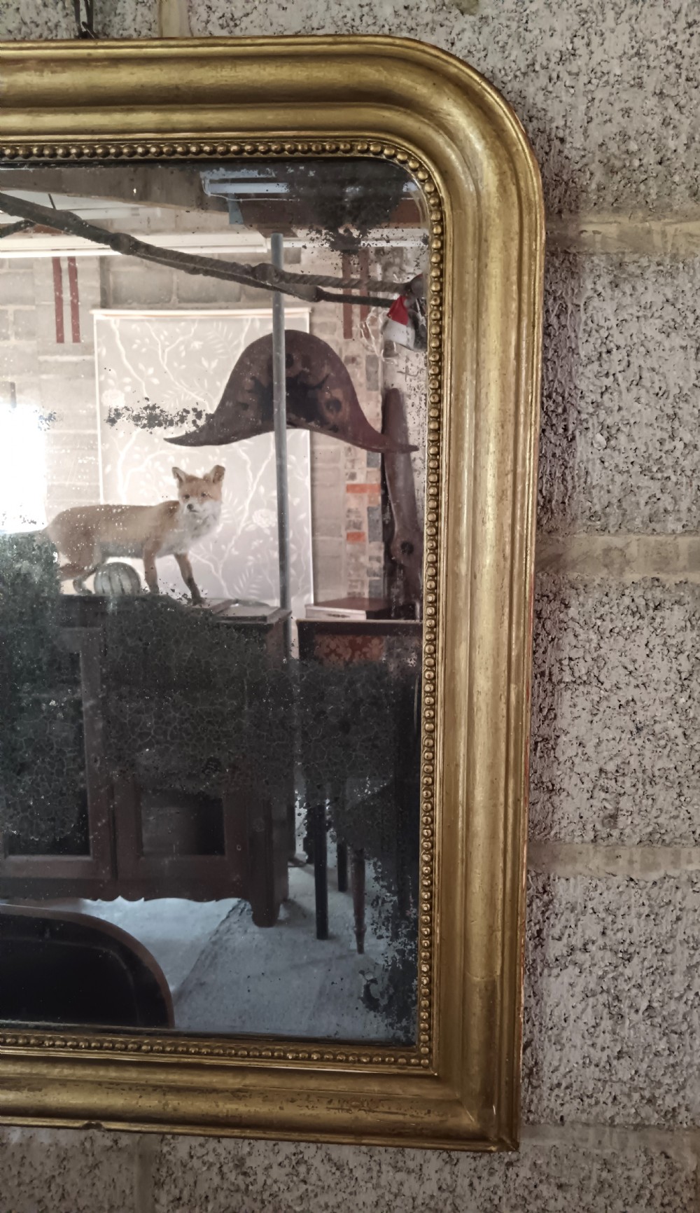 A 19th-century French wall mirror featuring a rectangular gilded frame with rounded upper corners, beaded interior moulding, and heavily foxed glass. View VII