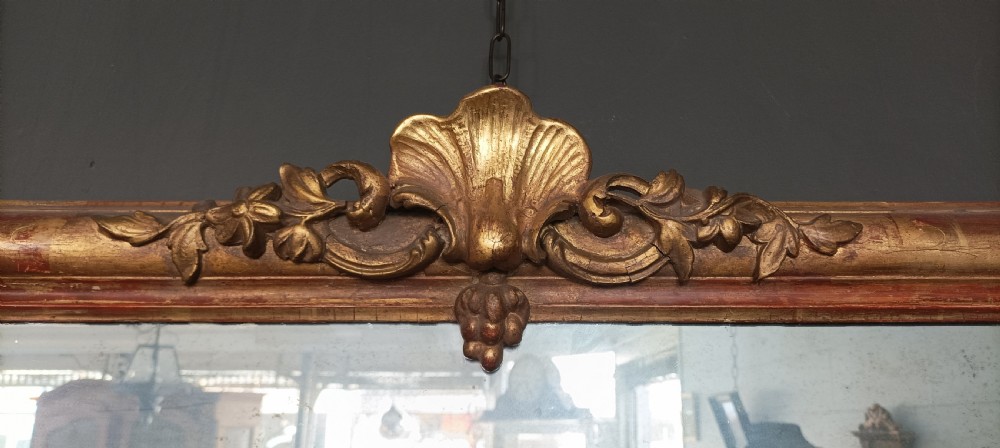 An antique gilded wood overmantel mirror featuring rounded top corners, a central carved shell crest, and scroll bracket feet. View VII