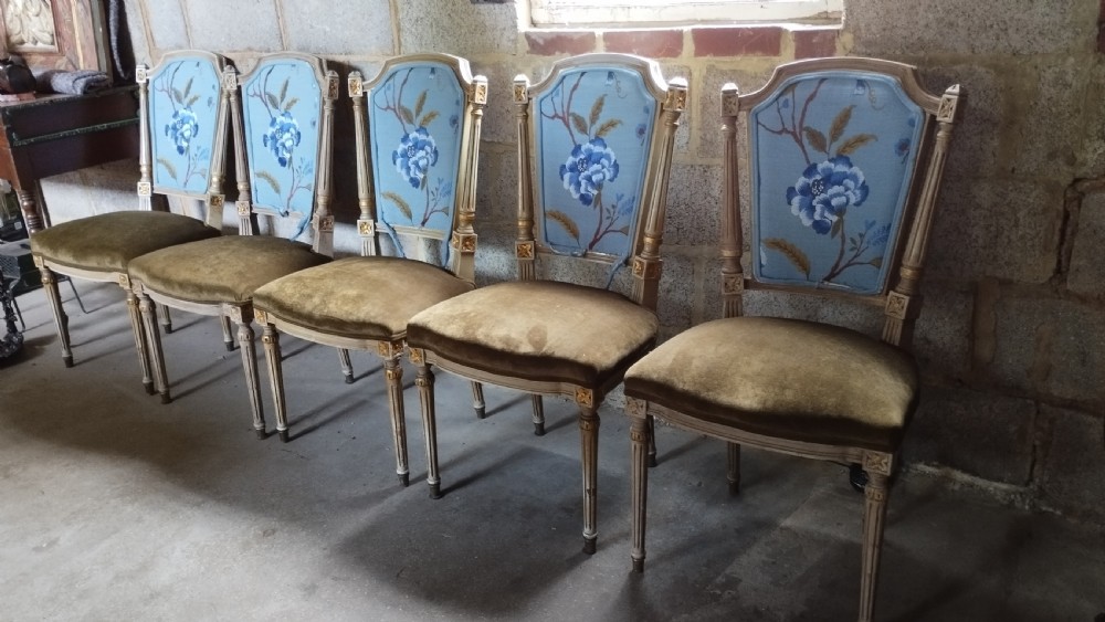 A set of five Louis XVI style dining chairs featuring carved painted wooden frames, floral blue upholstered backs, and olive green velvet seats.