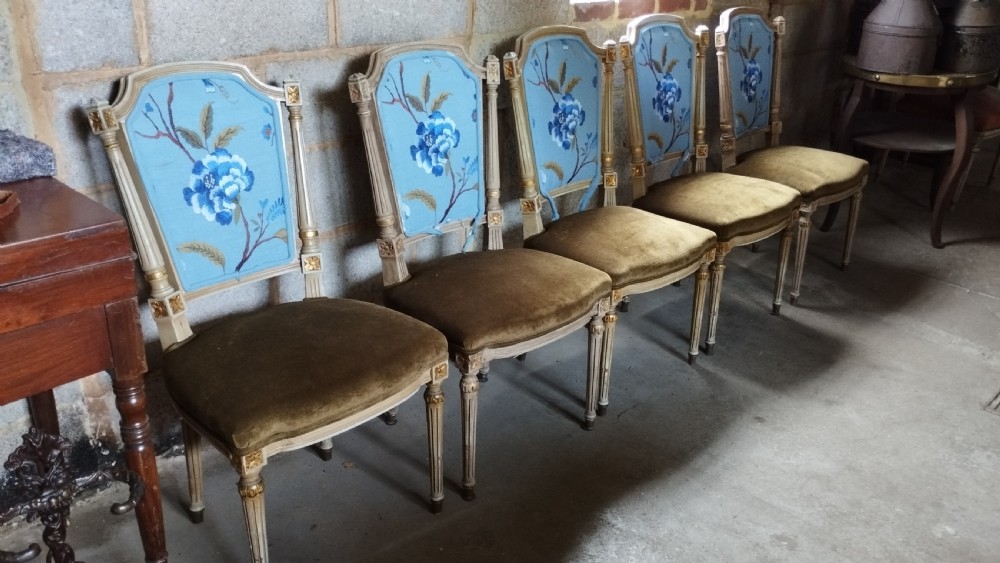A set of five Louis XVI style dining chairs featuring carved painted wooden frames, floral blue upholstered backs, and olive green velvet seats. View II