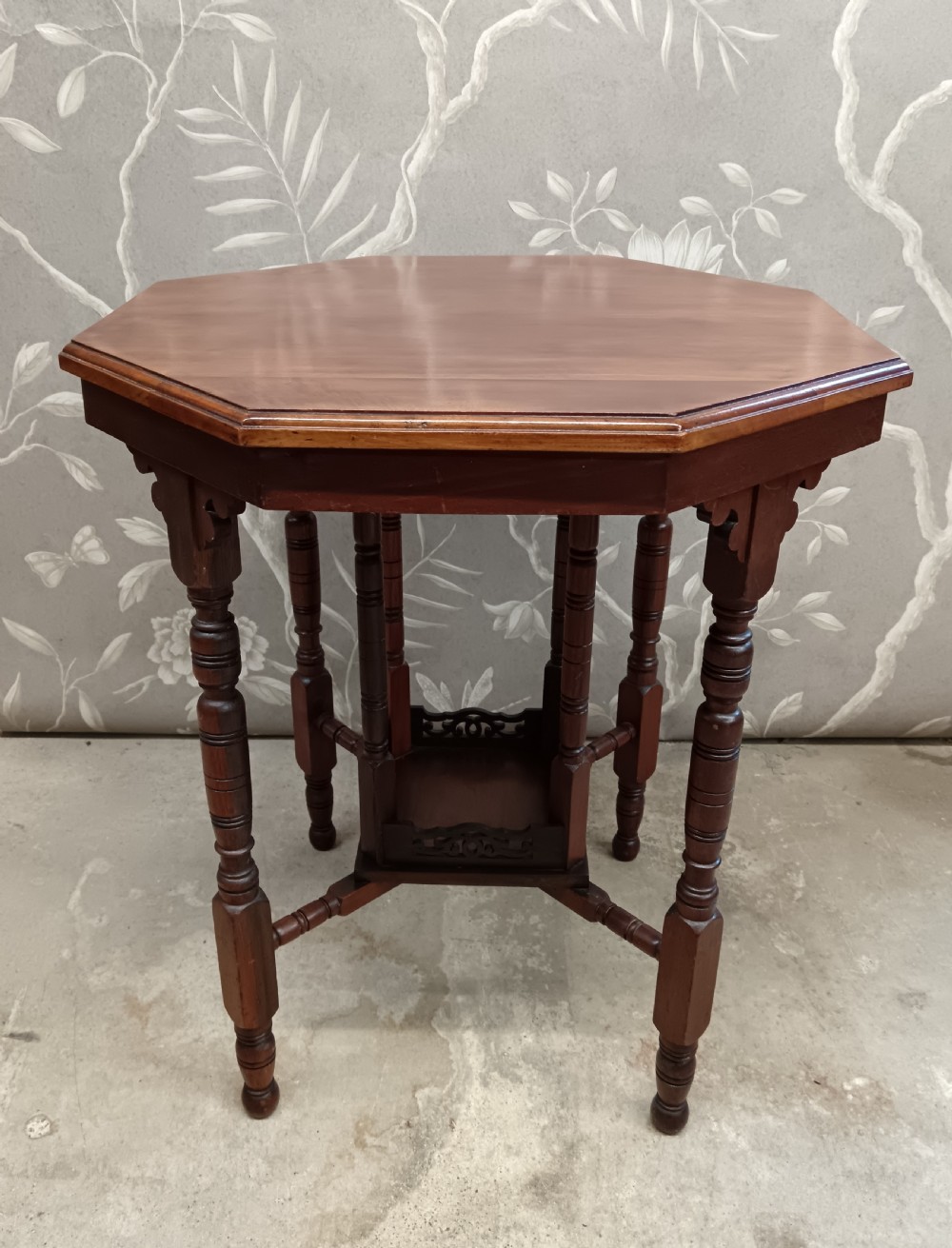 An octagonal dark walnut side table featuring turned legs, a lower shelf with decorative carved fretwork, and an eight-sided bevelled top.