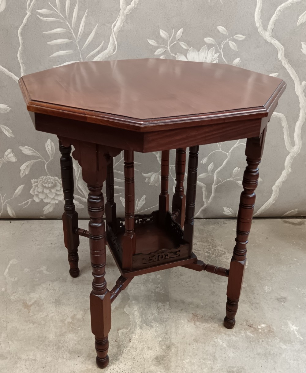 An octagonal dark walnut side table featuring turned legs, a lower shelf with decorative carved fretwork, and an eight-sided bevelled top. View VI