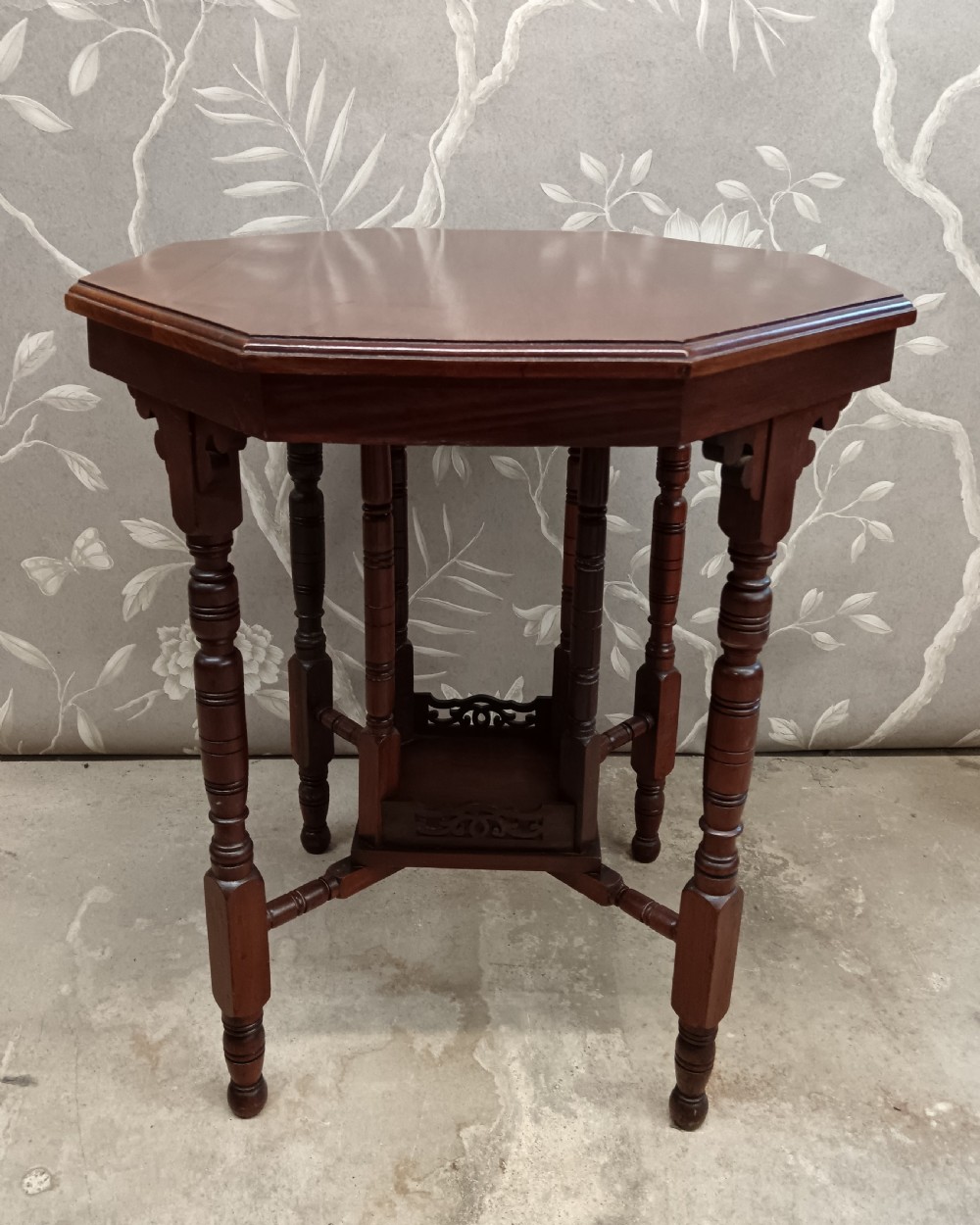 An octagonal dark walnut side table featuring turned legs, a lower shelf with decorative carved fretwork, and an eight-sided bevelled top. View VII