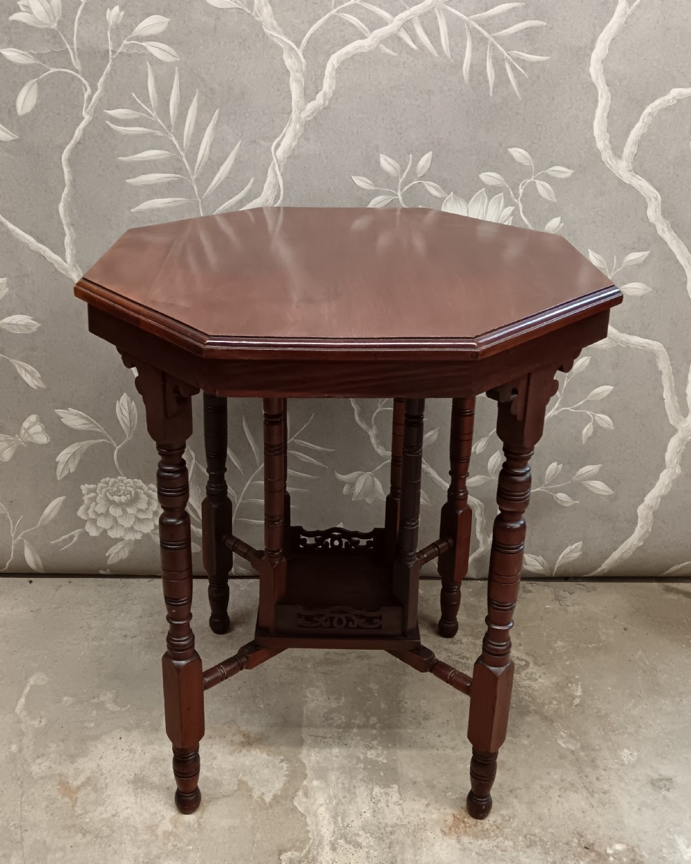 An octagonal dark walnut side table featuring turned legs, a lower shelf with decorative carved fretwork, and an eight-sided bevelled top. View VIII