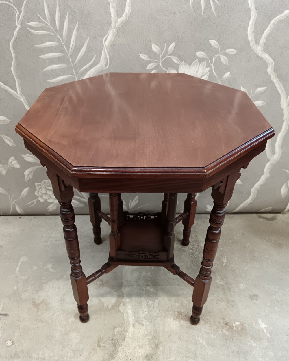 An octagonal dark walnut side table featuring turned legs, a lower shelf with decorative carved fretwork, and an eight-sided bevelled top. View IX