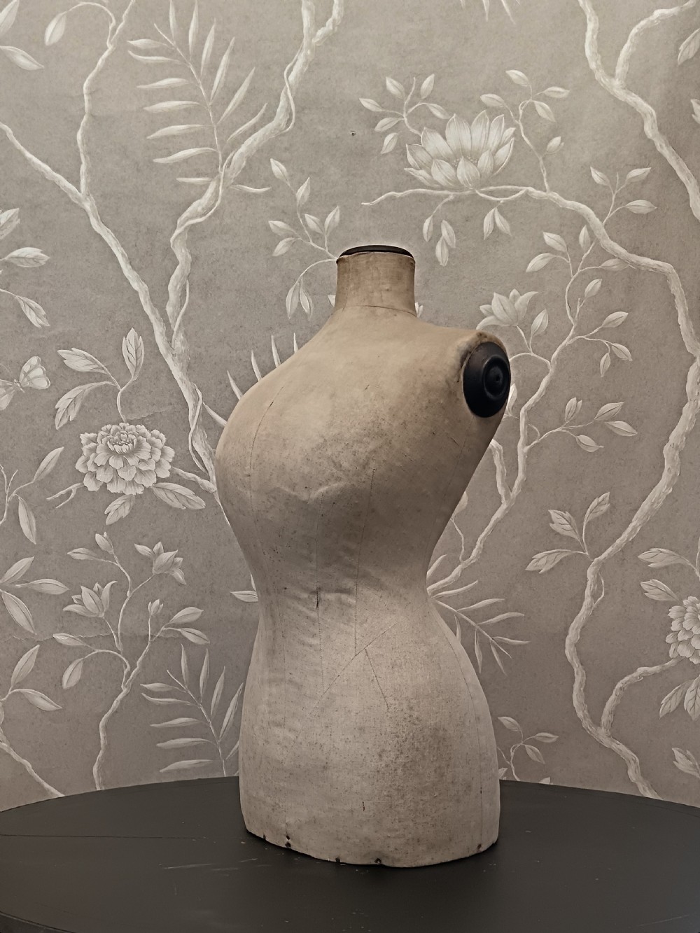 An aged cream fabric-covered female dressmaker torso mannequin bust with dark wood neck and shoulder caps.