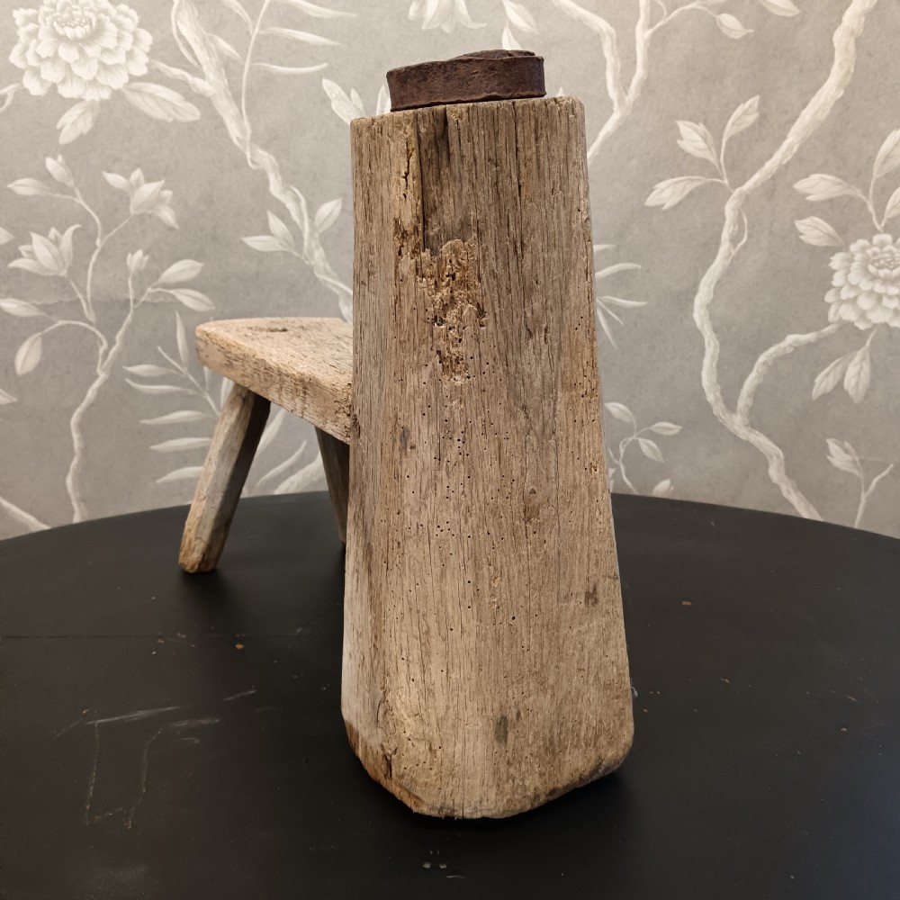 An early 19th-century wooden cobbler stool with a thick vertical timber post topped with iron, joined to a low horizontal bench surface with splayed legs. View III