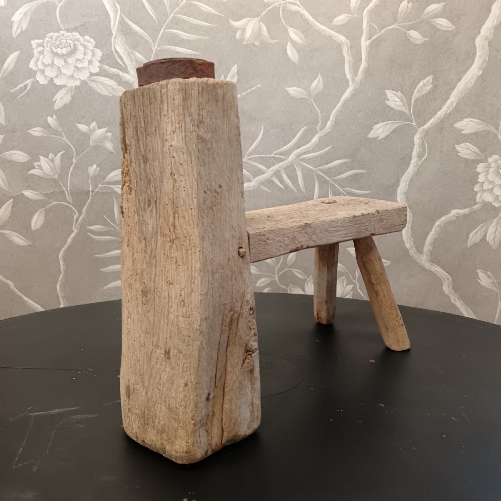 An early 19th-century wooden cobbler stool with a thick vertical timber post topped with iron, joined to a low horizontal bench surface with splayed legs. View V