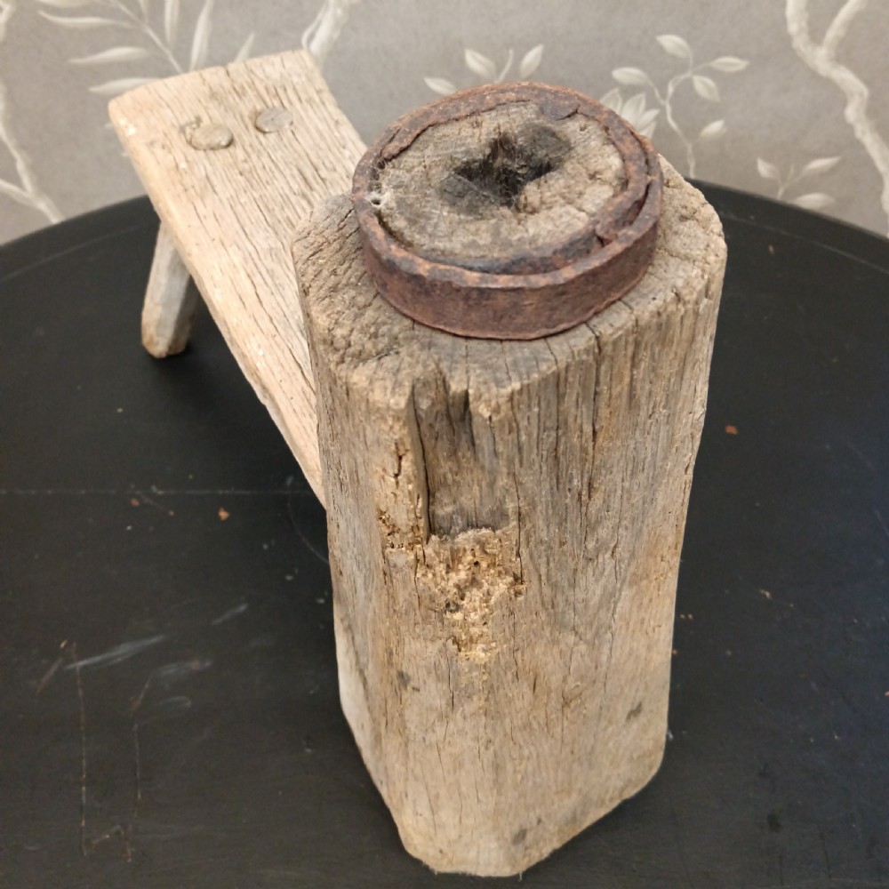 An early 19th-century wooden cobbler stool with a thick vertical timber post topped with iron, joined to a low horizontal bench surface with splayed legs. View VIII
