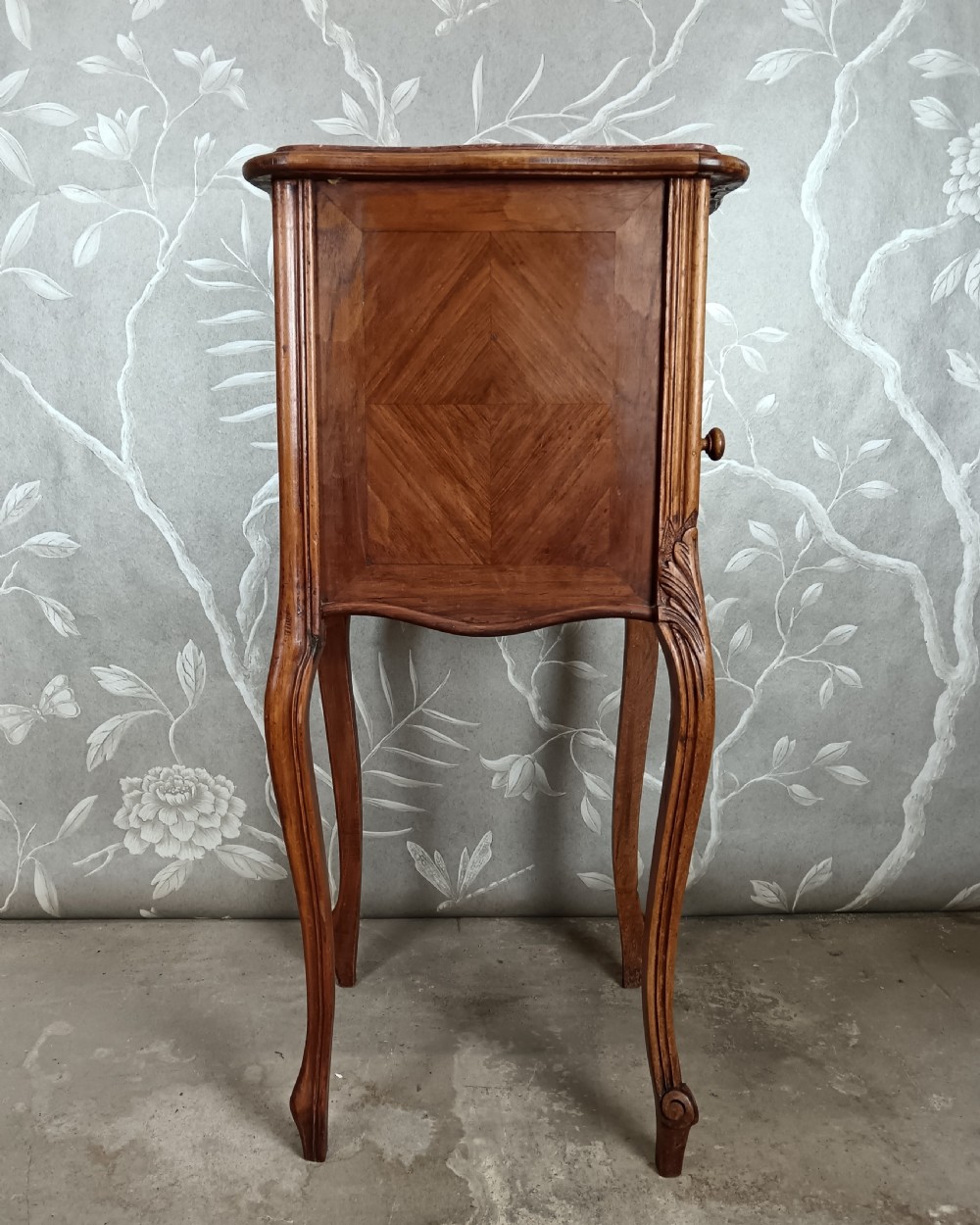 A tall French bedside cupboard crafted from warm brown wood with slim cabriole legs, parquetry panels, a single top drawer, and a lower cabinet door. View IV