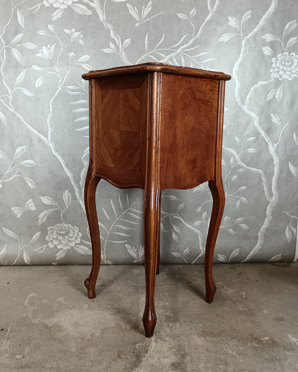 A tall French bedside cupboard crafted from warm brown wood with slim cabriole legs, parquetry panels, a single top drawer, and a lower cabinet door. View VI
