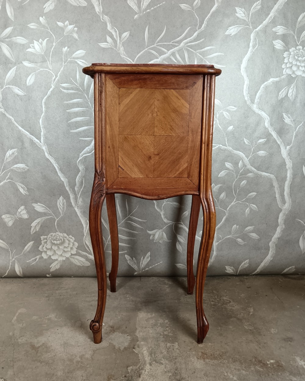 A tall French bedside cupboard crafted from warm brown wood with slim cabriole legs, parquetry panels, a single top drawer, and a lower cabinet door. View VII