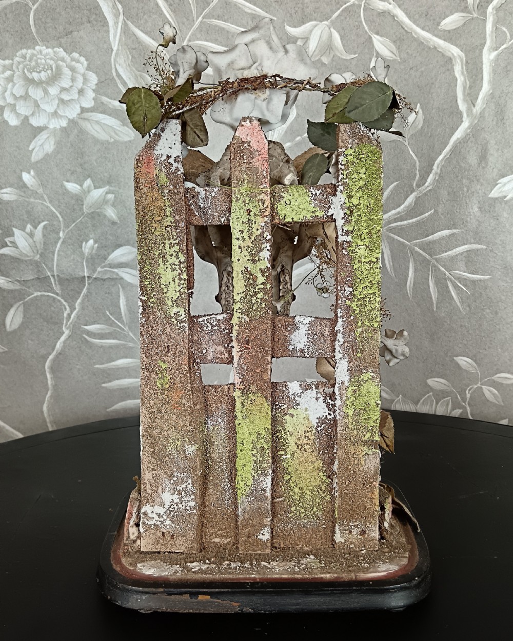 An antique Victorian animal skull with curved horns mounted on a moss-covered diorama base decorated with dried flowers, set upon a dark oval wooden plinth. View III