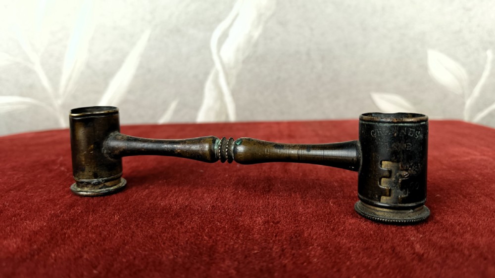 An antique French brass double-ended gunpowder measure featuring a turned central handle and stamped volumetric measurement graduations.