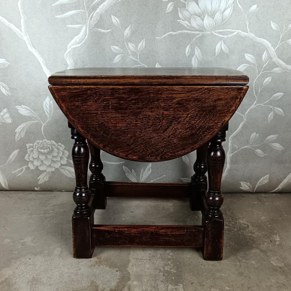 A dark oak coffee table featuring a drop-leaf swivel top supported by turned baluster legs and stretchers.