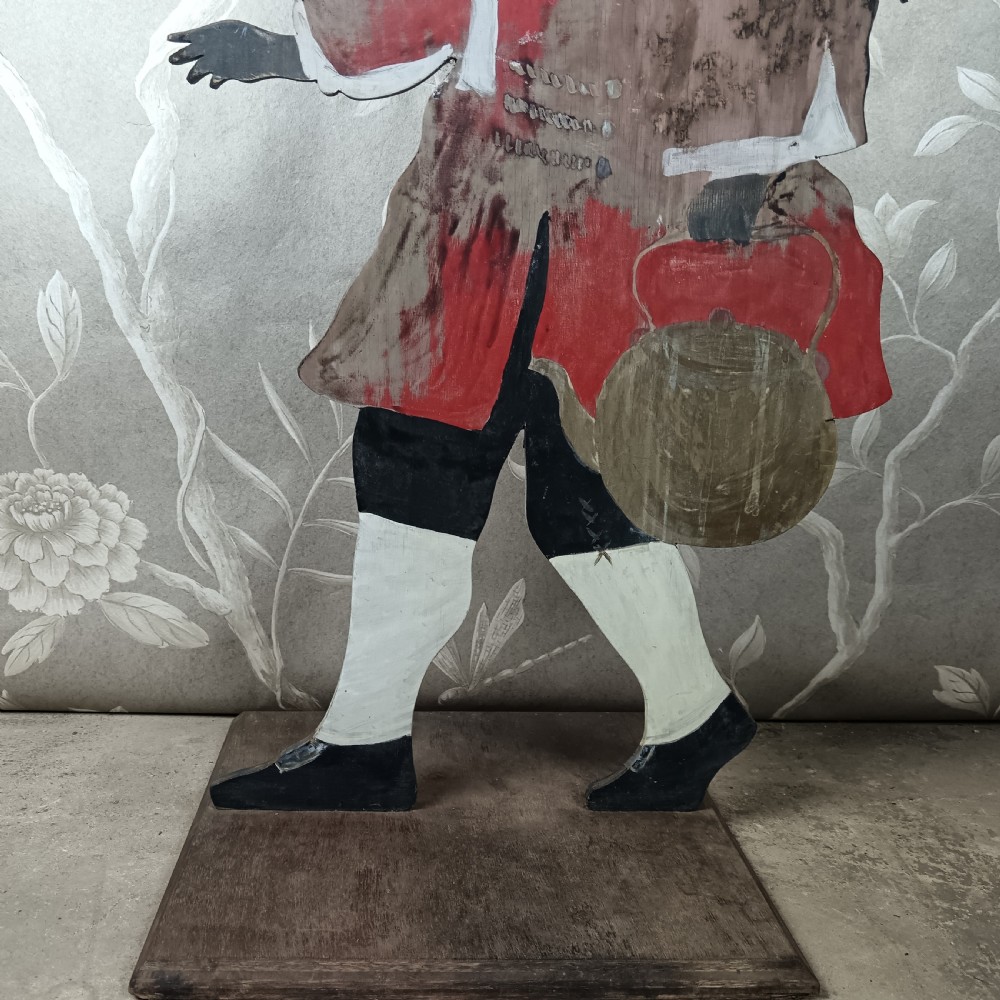 An early twentieth-century painted wooden dummy board figure depicting a man in a red coat and feathered hat holding a kettle. View IV