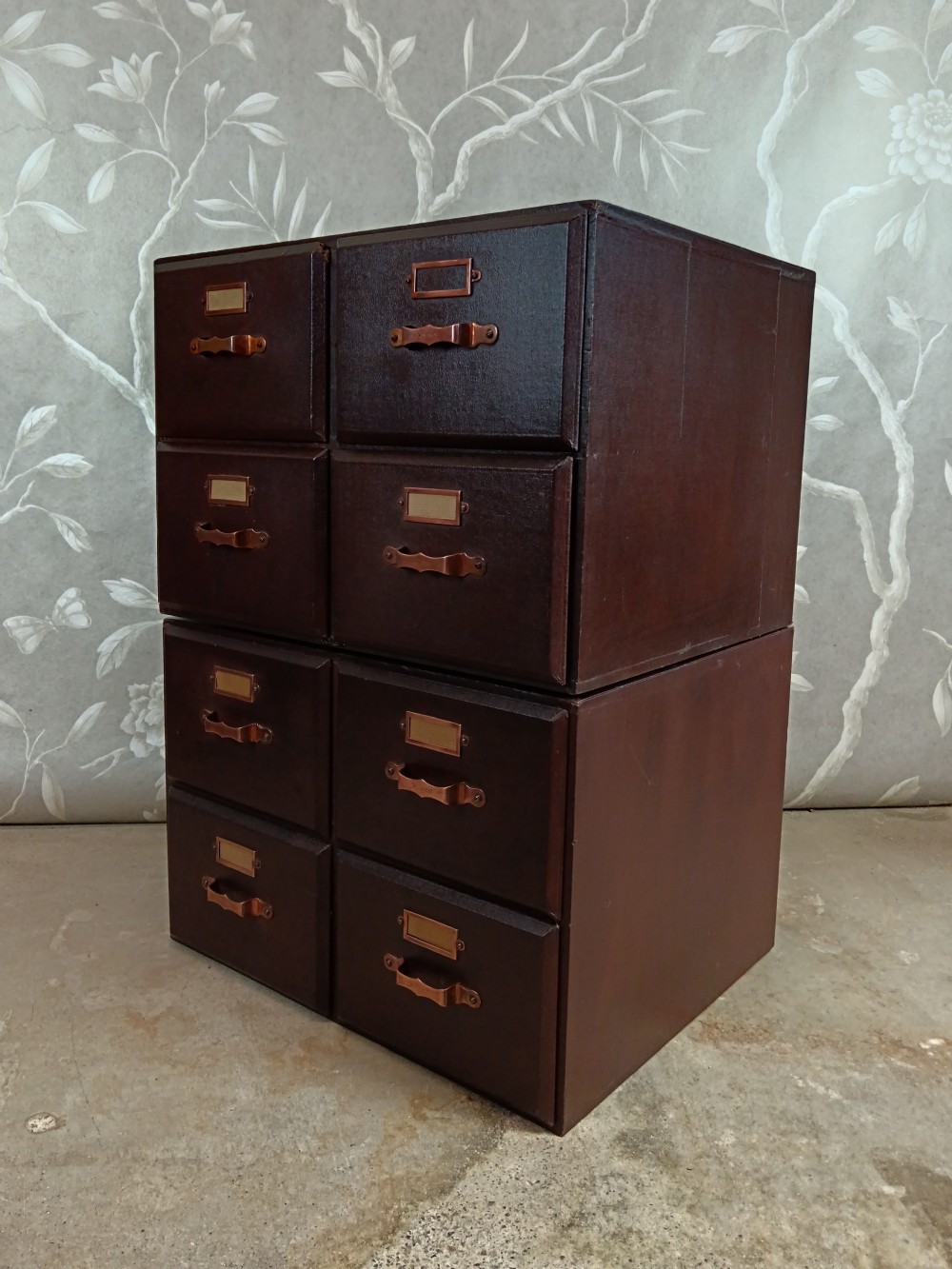 A dark brown modular card index filing cabinet featuring multiple drawers with copper handles and metal label holders. View III