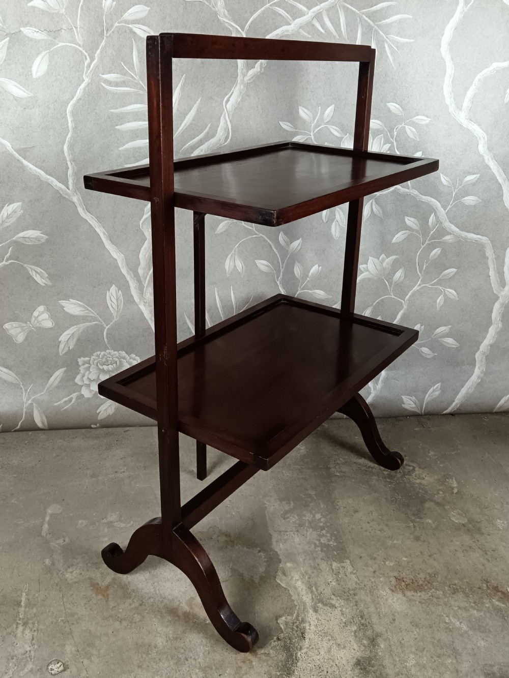 A dark mahogany two-tier folding dumb waiter with rectangular tray surfaces, upper carrying handle, and splayed legs. View VII