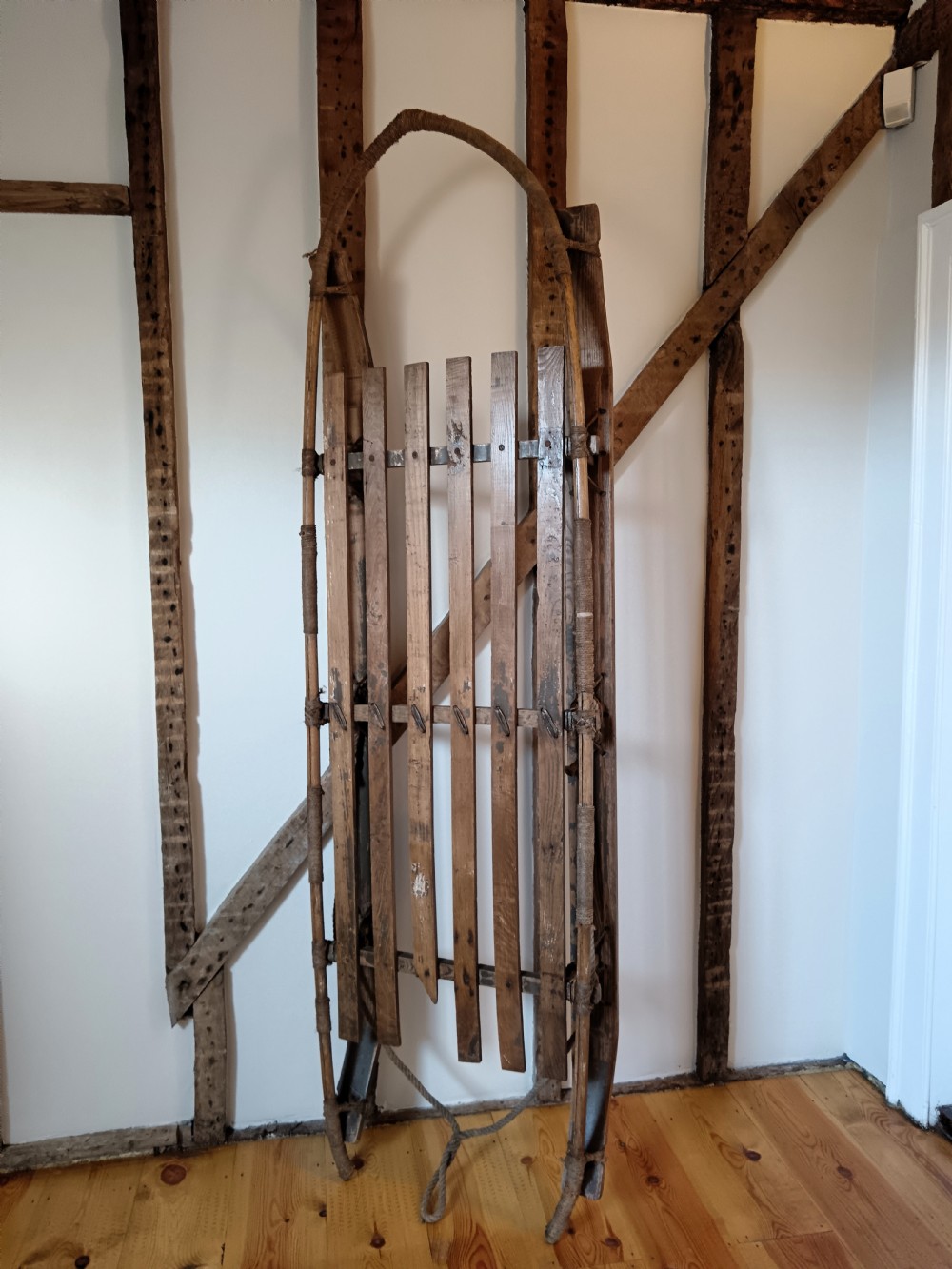 An antique Nansen-style polar expedition sledge constructed from timber slats bound with cordage on curved wooden runners. View II