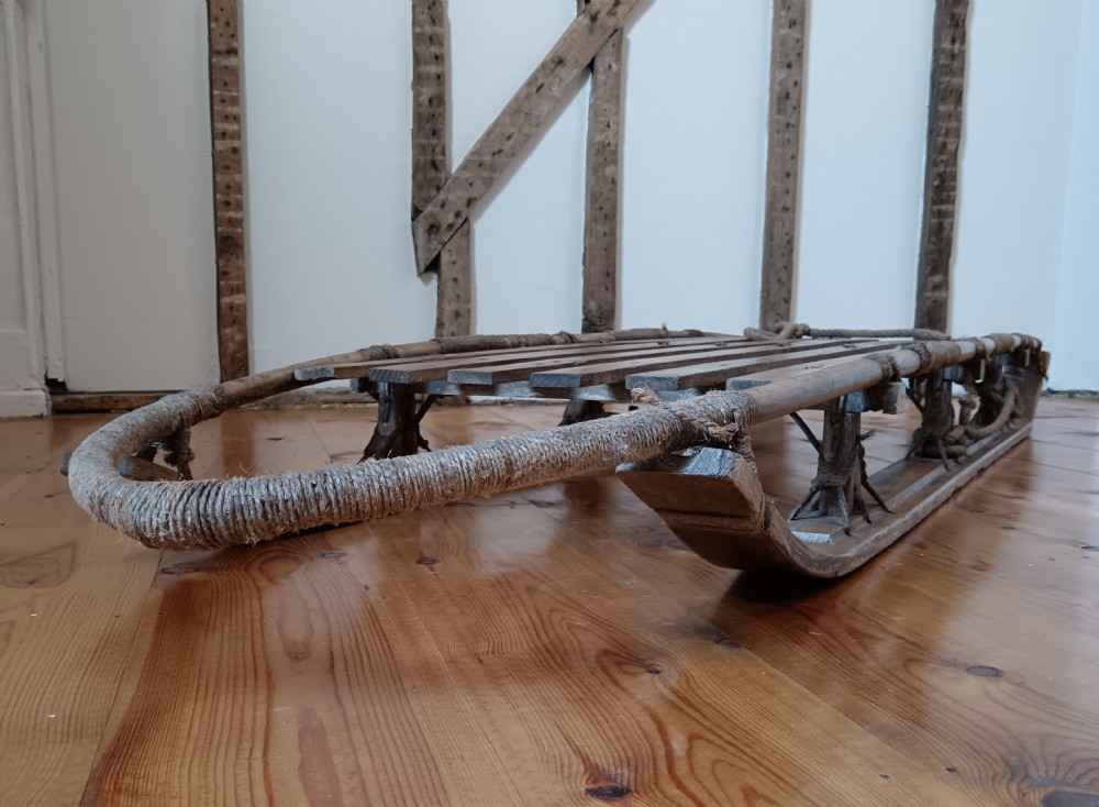 An antique Nansen-style polar expedition sledge constructed from timber slats bound with cordage on curved wooden runners. View IV